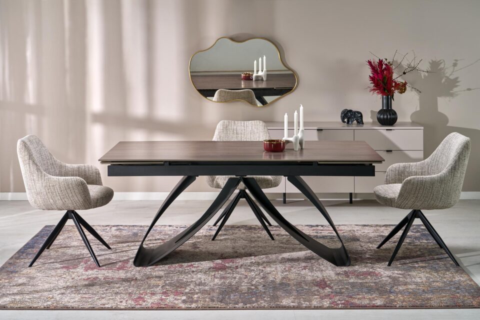 Raztegljiva jedilniška miza Hilario z leseno ploščo v odtenku črna/oreh in črnim podnožjem, postavljena na preprogo v jedilnici.